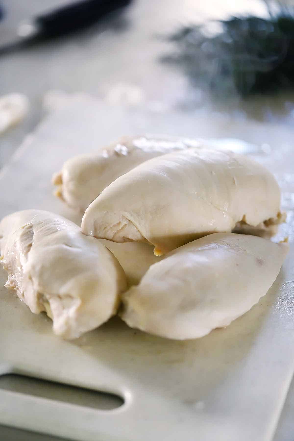 Whole poached chicken breasts on a cutting board.