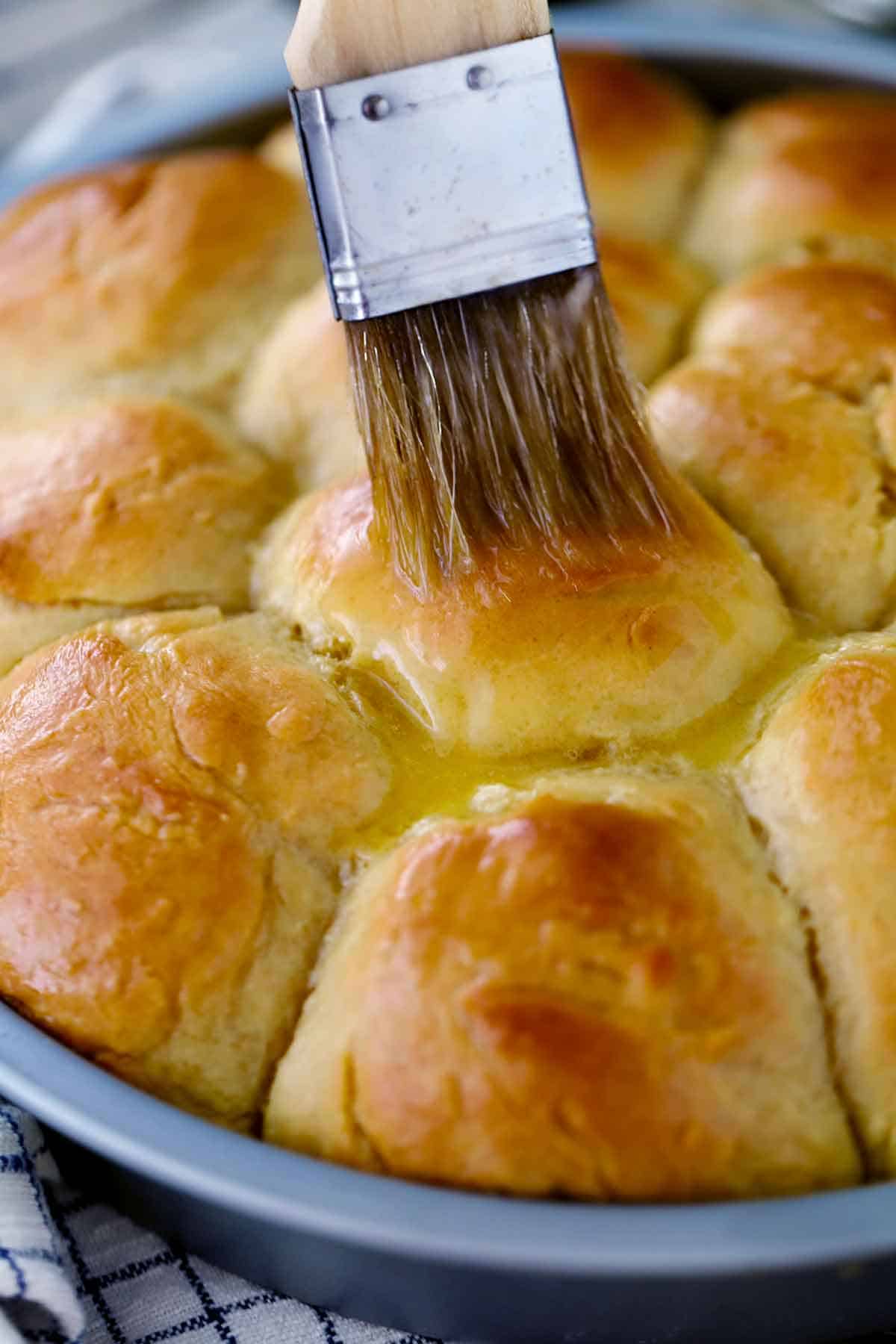Using a pastry brush to brush melted butter on baked dinner rolls.