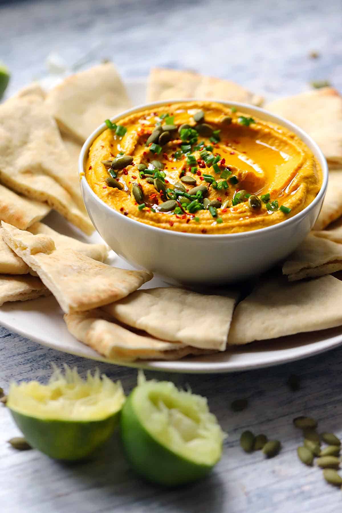 Side view of pumpkin hummus with squeezed lime halves in the foreground.