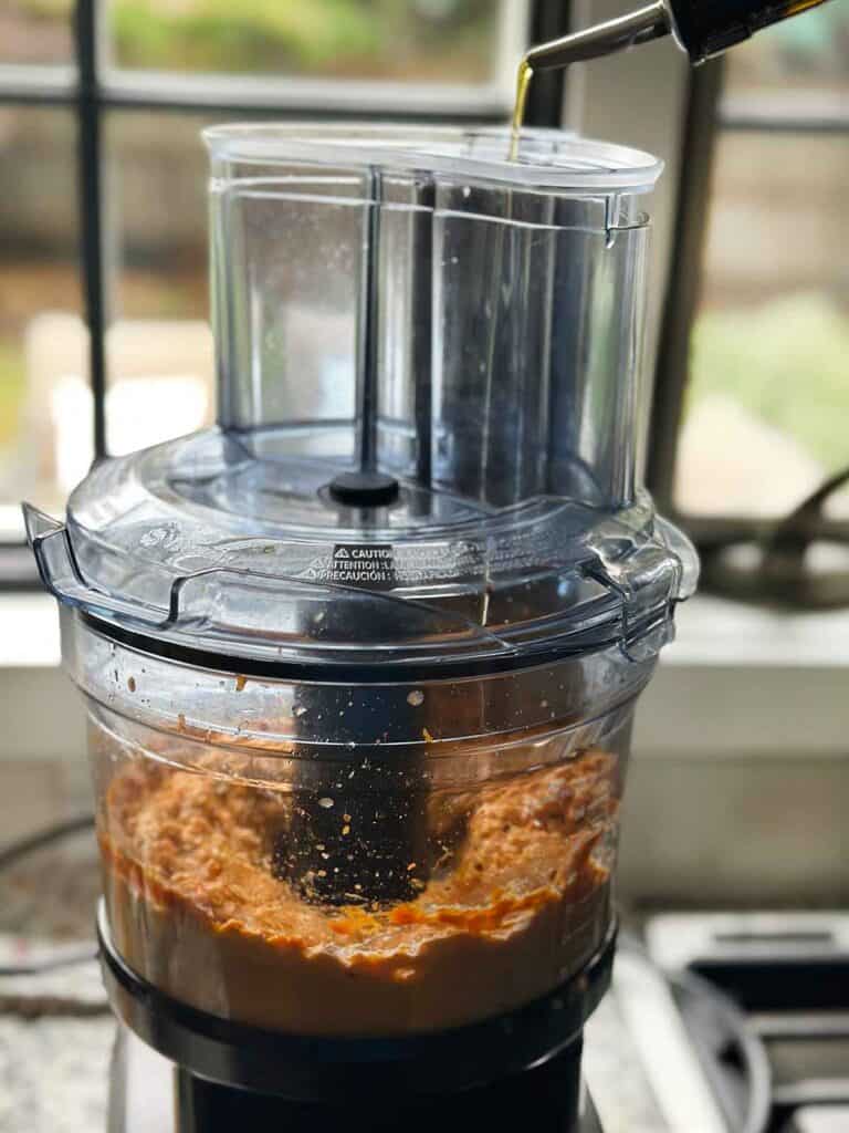 Drizzling olive oil into a running food processor with hummus.