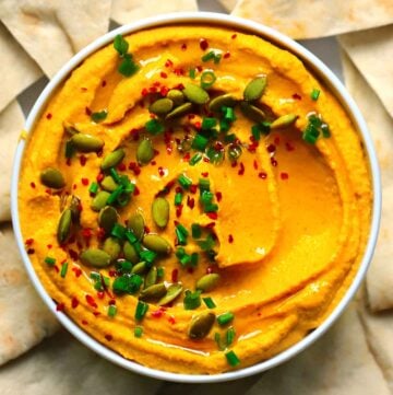 Square close up photo of an overhead view of pumpkin hummus with curry topped with chives, pumpkin seeds, olive oil, and Aleppo pepper.