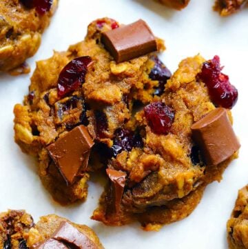 Square photo of a pumpkin oatmeal cookie broken in half with chocolate chunks and cranberries.