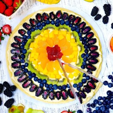 Square photo of rainbow fruit pizza with a slice taken out.