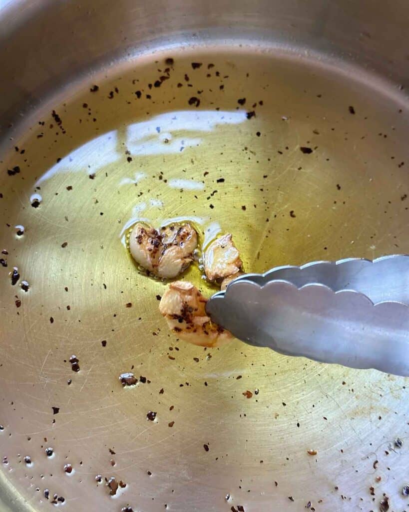 Removing toasted garlic cloves from oil in a skillet.