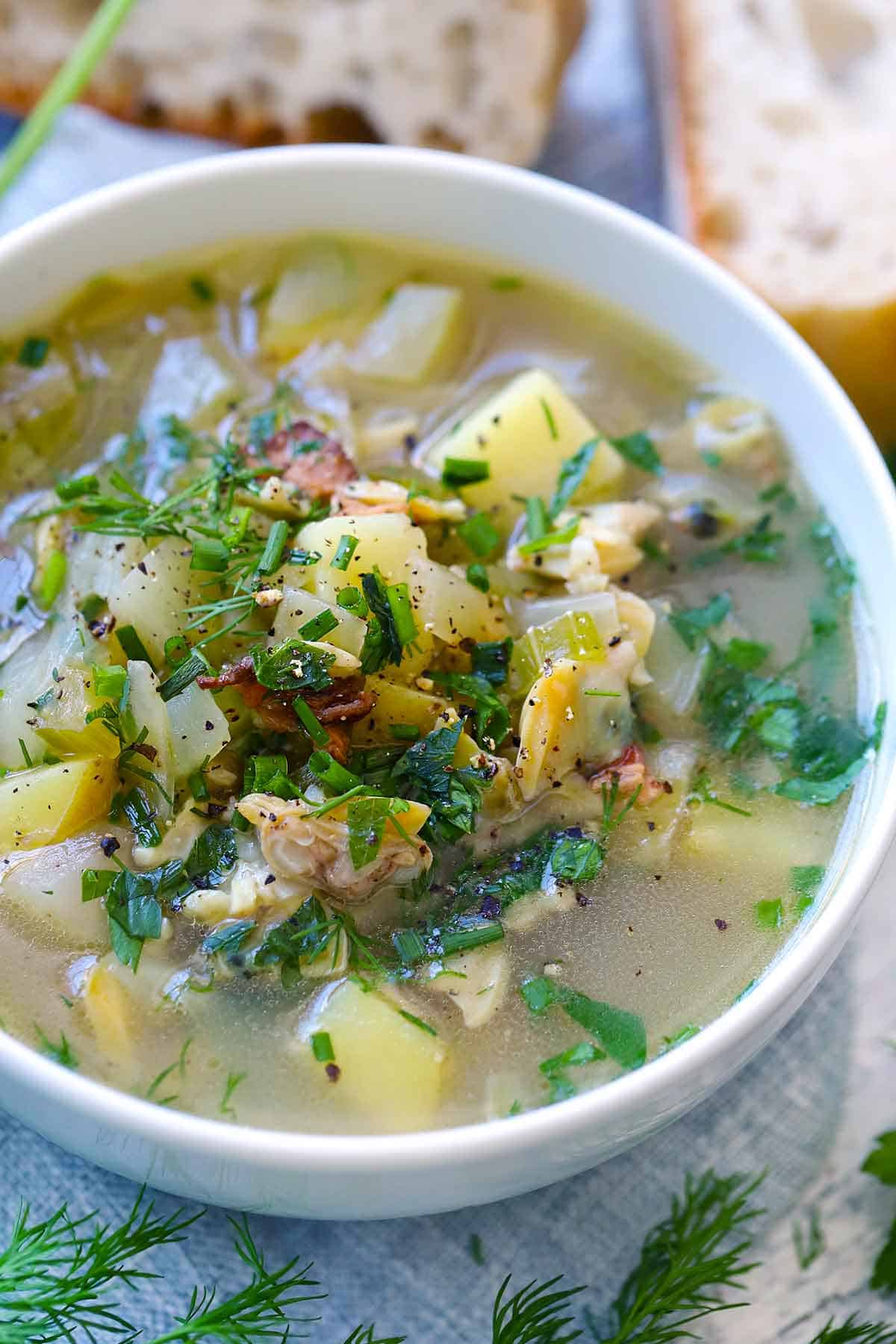 Close up side view of clear broth Rhode Island clam chowder topped with fresh herbs and black pepper.