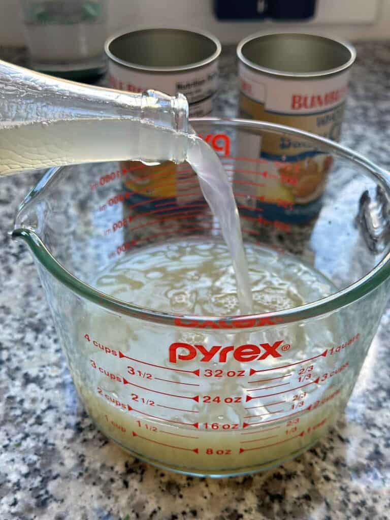 Measuring out jarred clam juice into a 4-cup glass measuring cup.