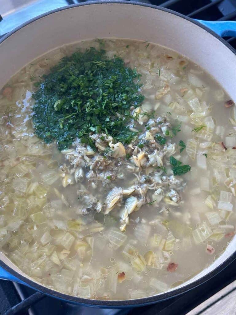Adding fresh herbs and canned clams to chowder in a Dutch oven.