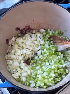 Adding celery and onions to a Dutch Oven with bacon.