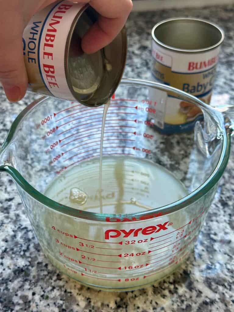 Draining juice from canned clams into a 4-cup glass measuring cup.