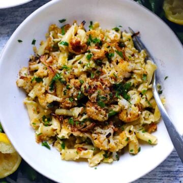 Square photo of overhead view of roasted cauliflower pasta topped with parsley and crispy breadcrumbs.