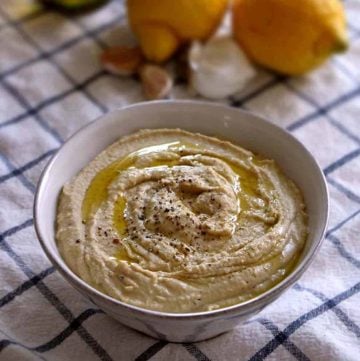 Bowl of hummus on blue and white checkered tablecloth.