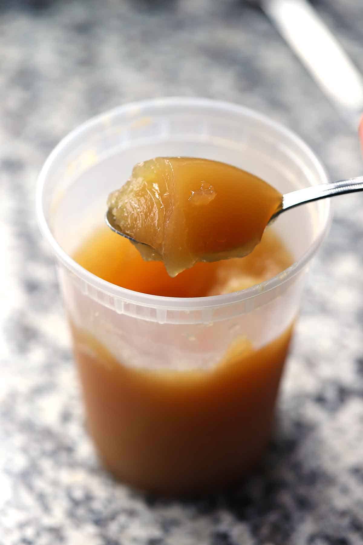 A spoon scooping out some homemade chicken bone broth made from rotisserie chickens that has gelled up from the high collagen.