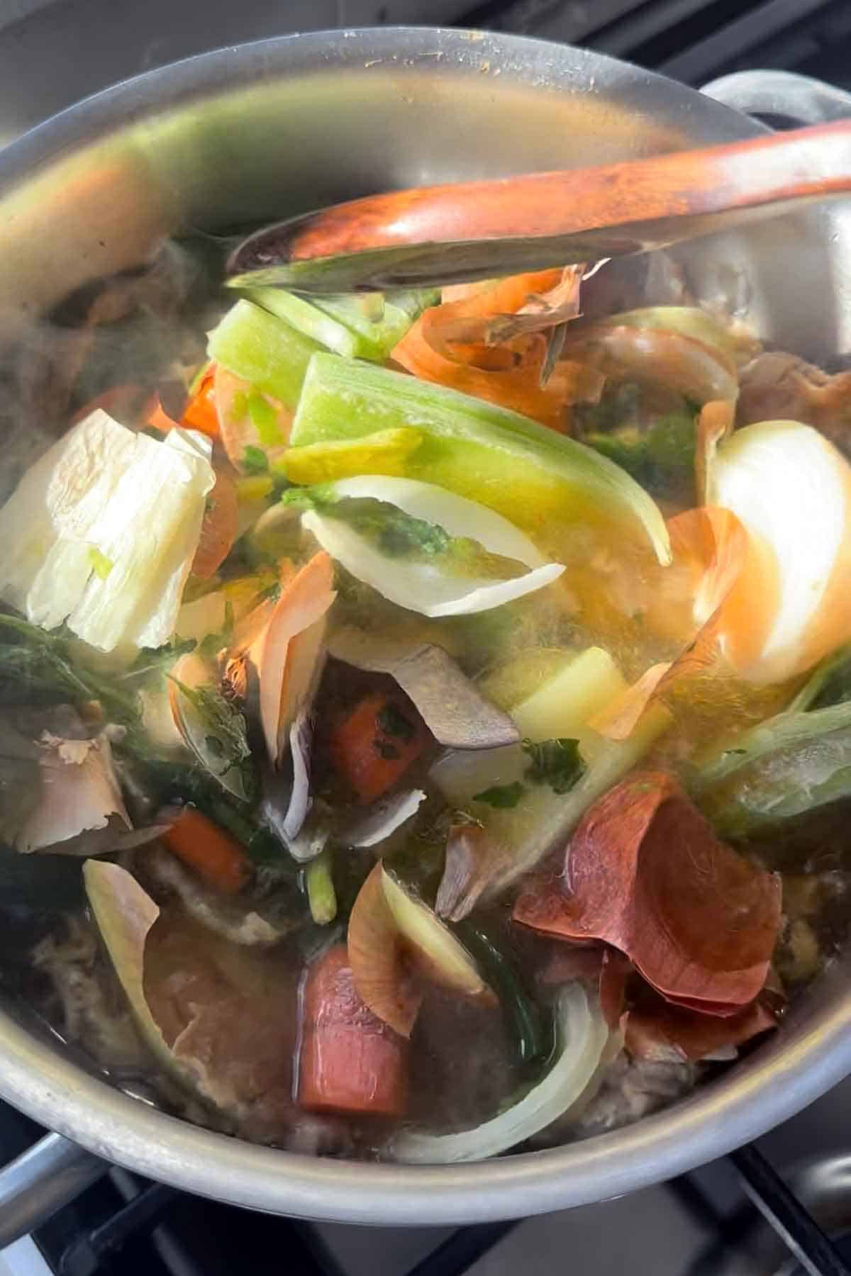Adding frozen vegetable scraps from celery, onions, and carrots to a pot of homemade chicken broth.