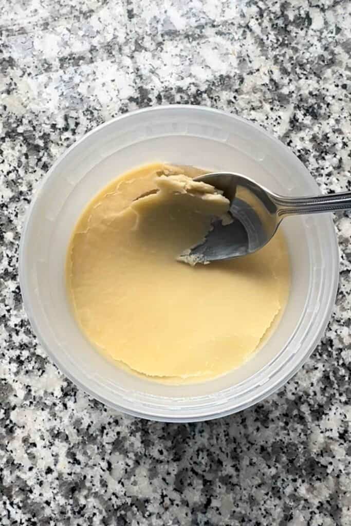 Spooning the fat off the top of homemade chicken broth, which has solidified after cooling, making it easy to remove.