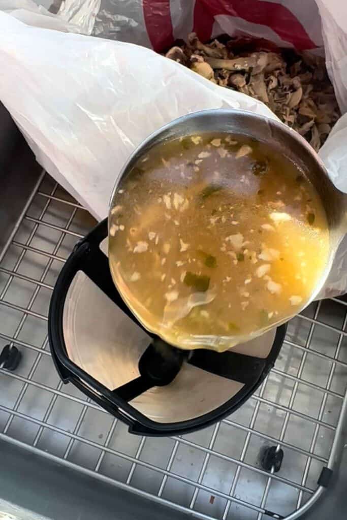 Straining homemade chicken broth into a container through a coffee filter.