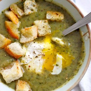 Bird's eye view of a bowl of green soup topped with croutons and an egg, with a spoon perched on the edge of the bowl.