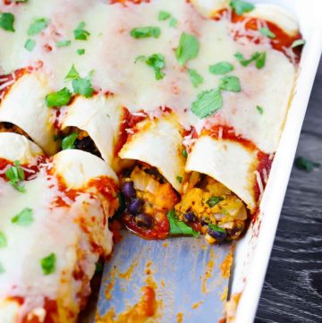 A close up shot of sweet potato black bean enchiladas topped with cilantro in a white baking dish.