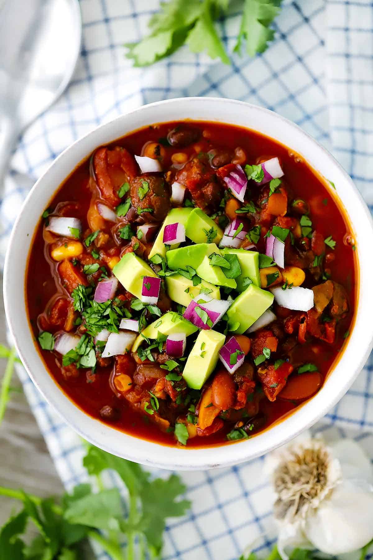 An overhead photo of a bowl of vegetarian chili with diced avocado, cilantro, and red onion on top.