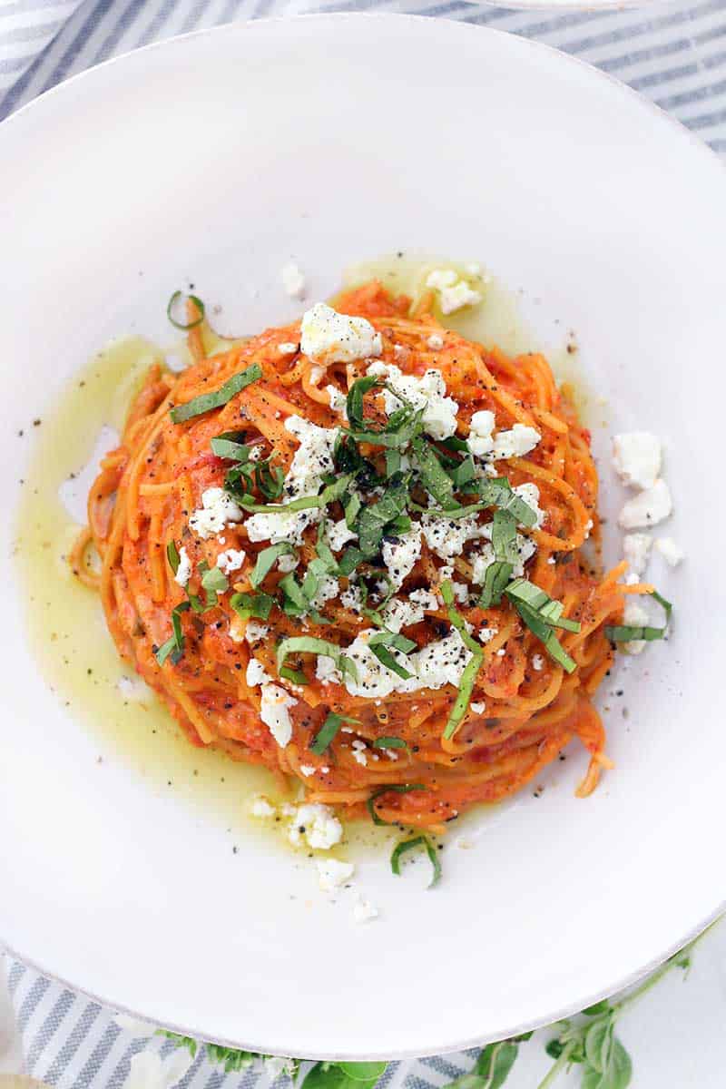 A plate of spaghetti with roasted red pepper sauce, goat cheese, and a chiffonade of basil