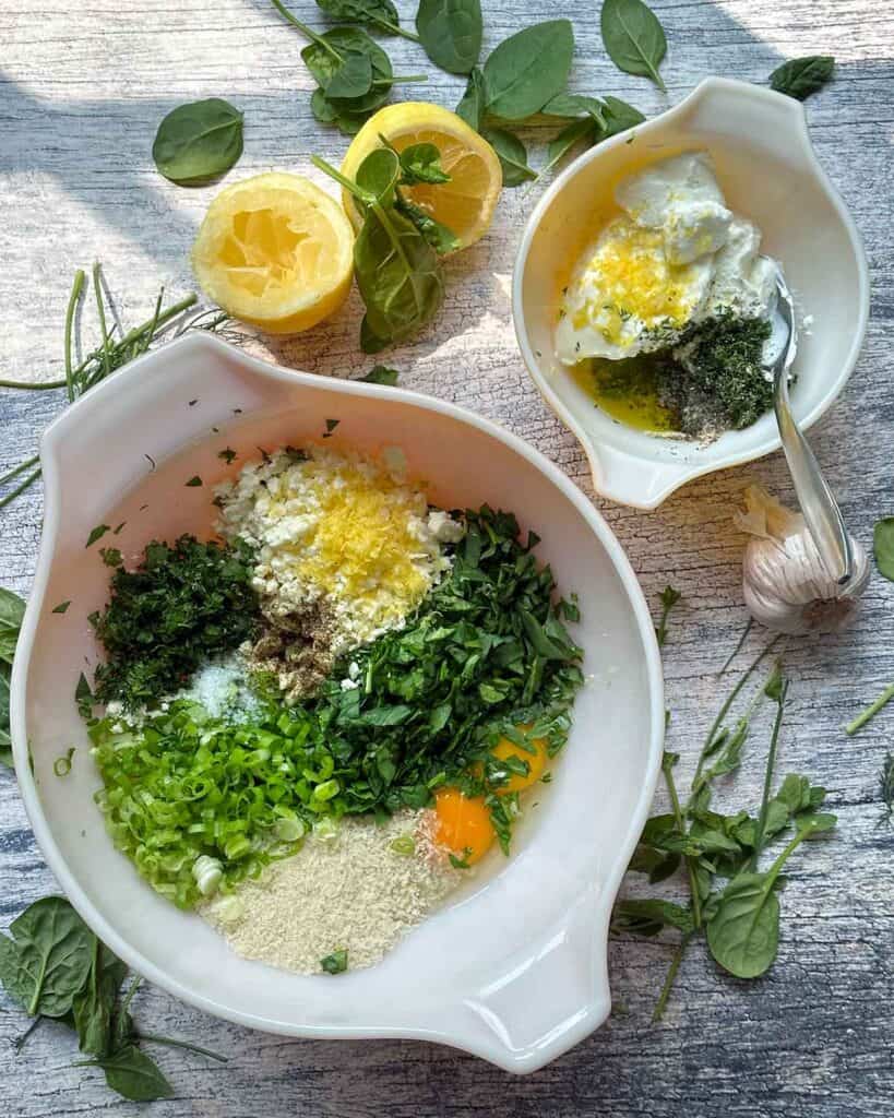 Overhead photo of two bowls with ingredients for spanakopita turkey burgers and a yogurt lemon garlic herb sauce.