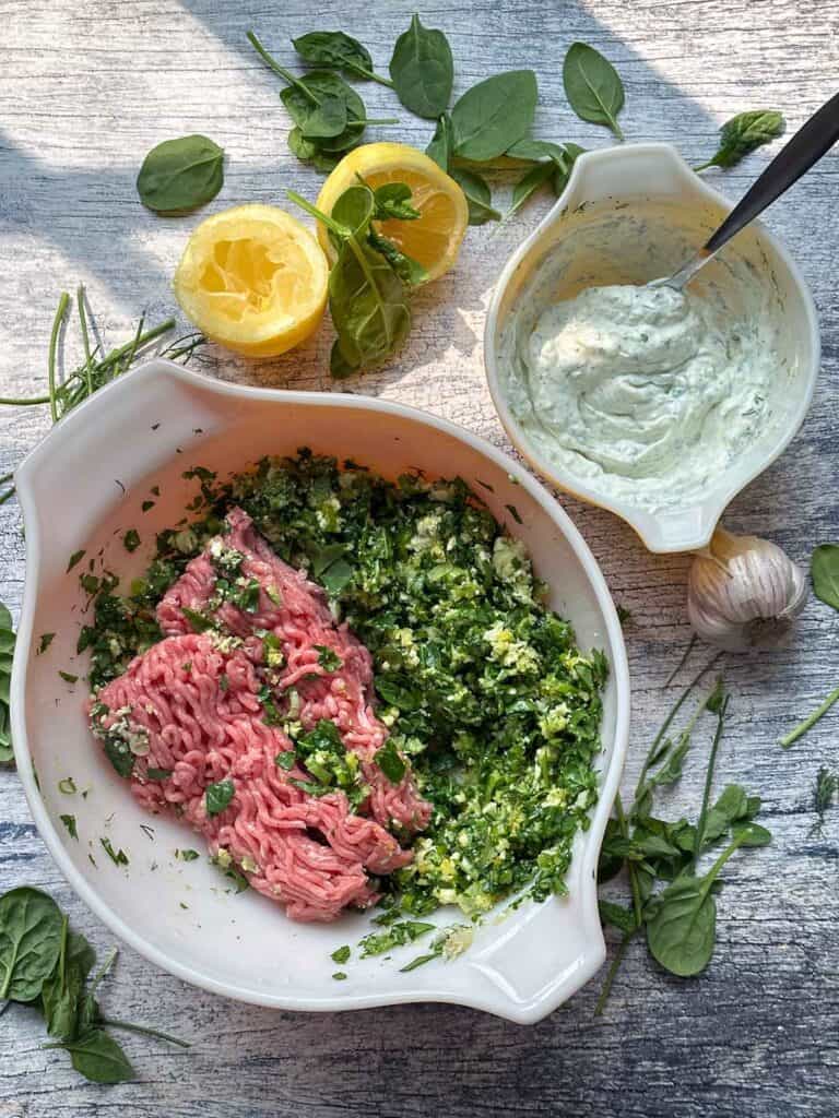 Overhead photo of two bowls, one with a mixture for spanakopita turkey burgers and the other with a mixture for a garlic herb yogurt sauce.