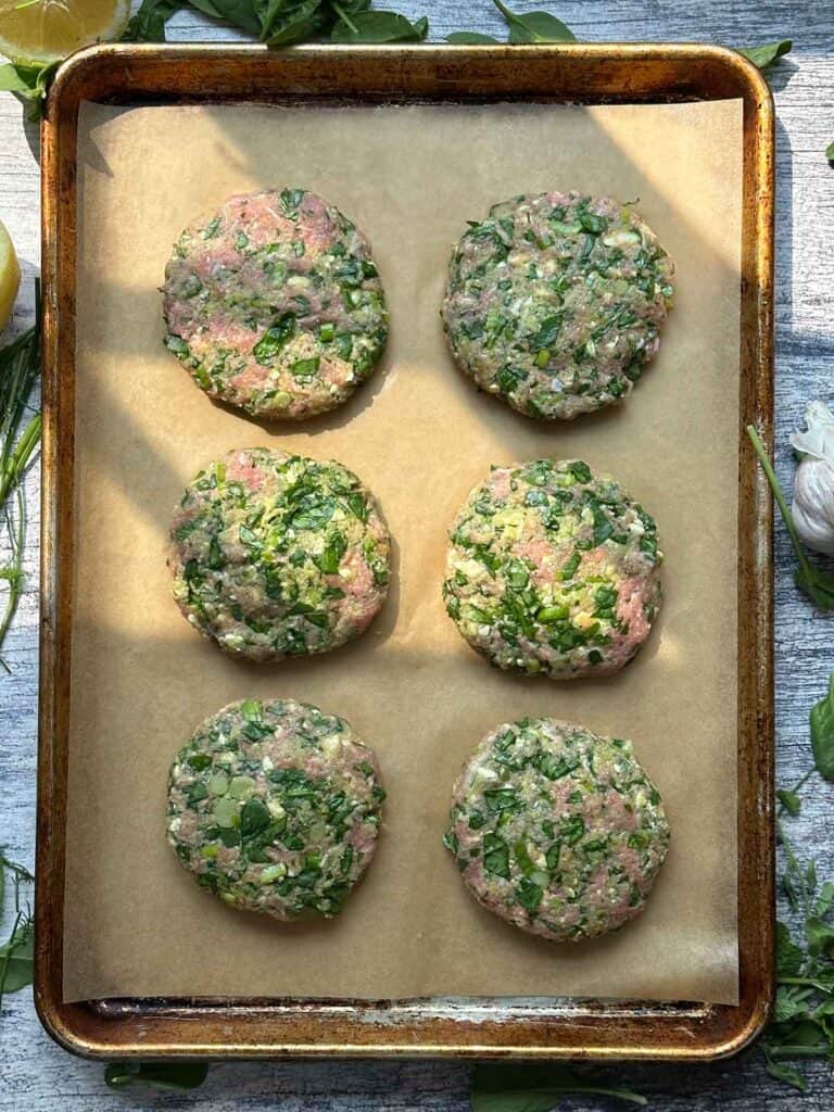 Overhead photo of six spanakopita turkey burger patties on a baking sheet on parchment paper ready to go in the oven.