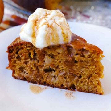 Square photo of spiced apple cake on a white plate with whipped cream and glaze on top.