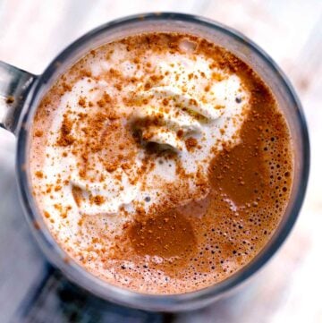 Square photo of a mug of spicy hot chocolate with whipped cream and cinnamon from above.