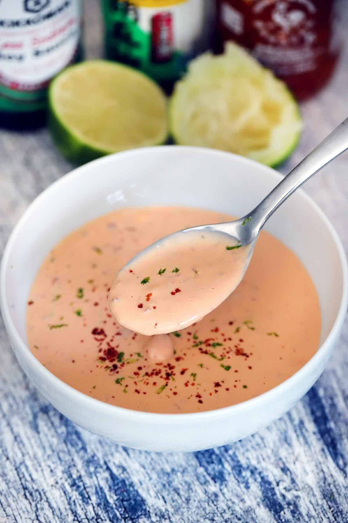 A spoon taking a spoonful of spicy mayo out of a white bowl.