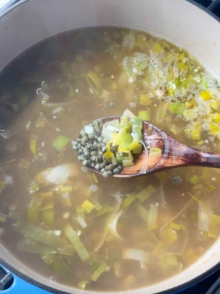 Adding broth and green lentils to soup with leeks and garlic.