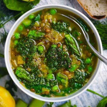 Square photo of an overhead view of spring lentil vegetable soup with bright green veggies and herb pistou spooned on top.