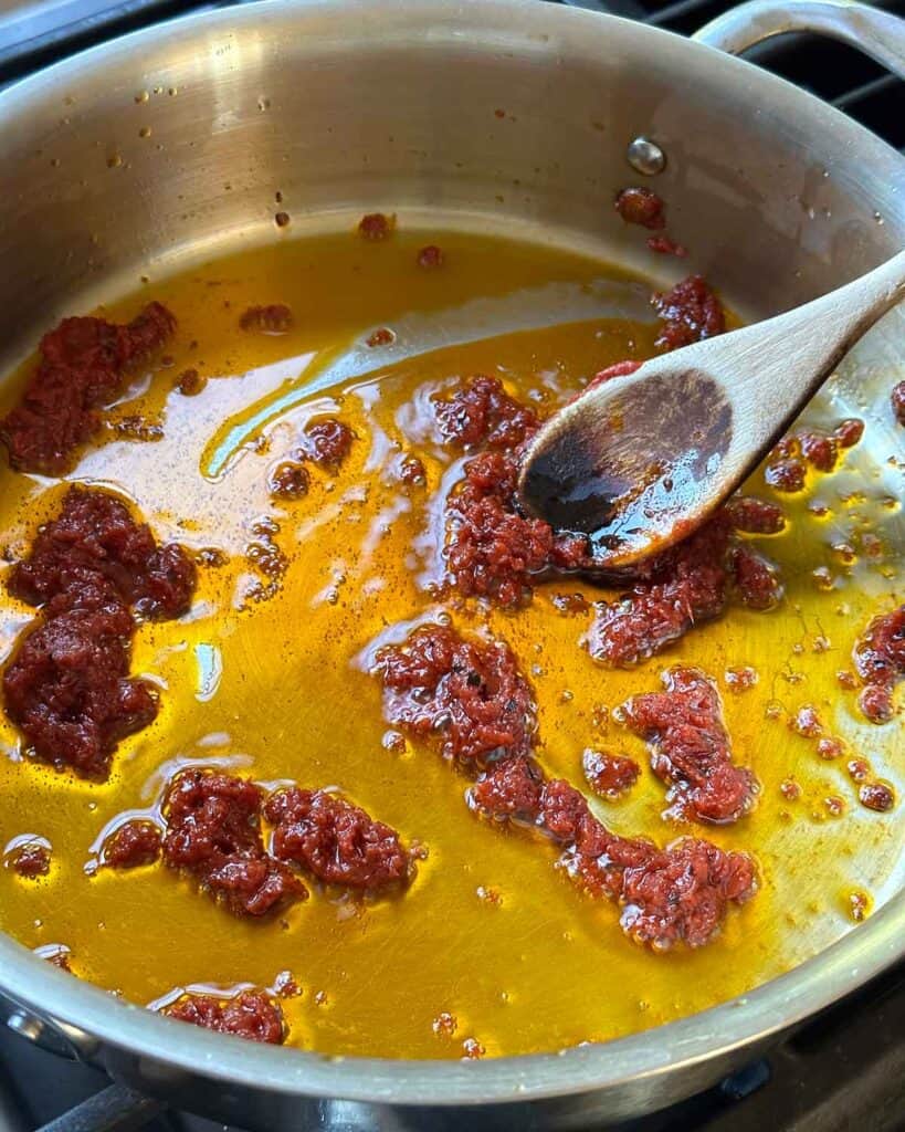 Stirring tomato paste in a skillet in olive oil.