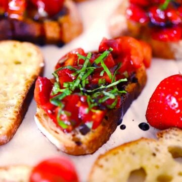 Square photo of strawberry bruschetta on a crostini with fresh basil garnish.
