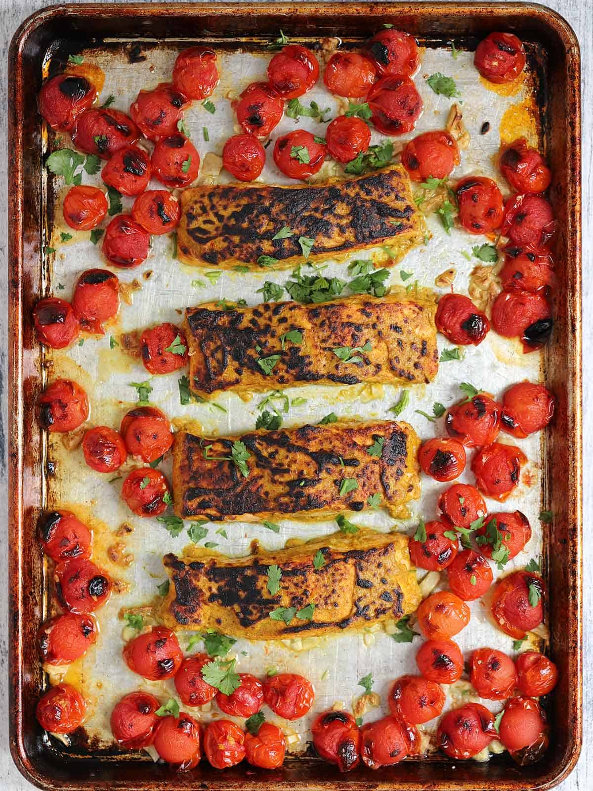Tandoori salmon and cherry tomatoes on a sheet pan after being broiled in the oven.