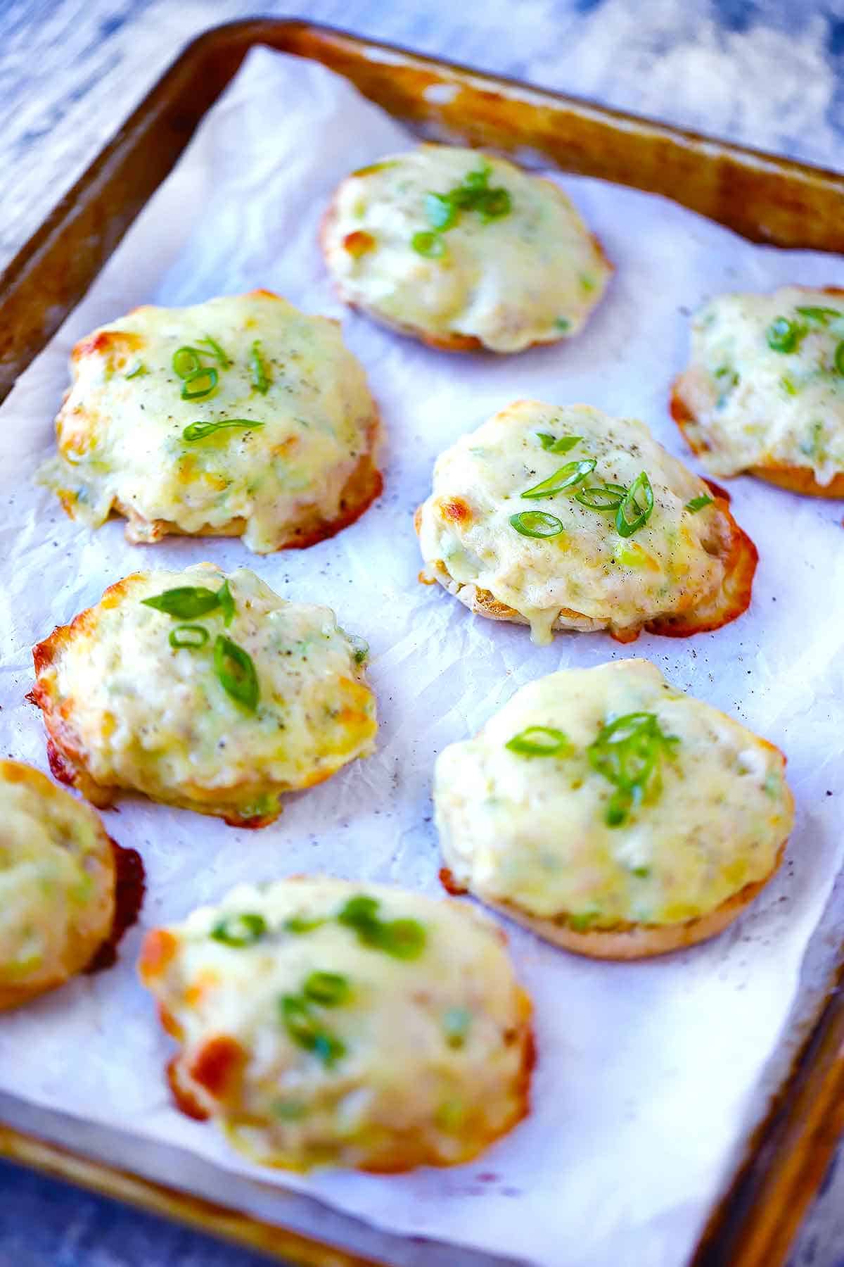 A baking sheet with English muffin tuna melts on it.