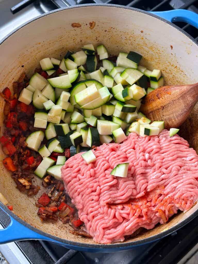 Adding chopped zucchini and ground turkey to a pot to make chili.