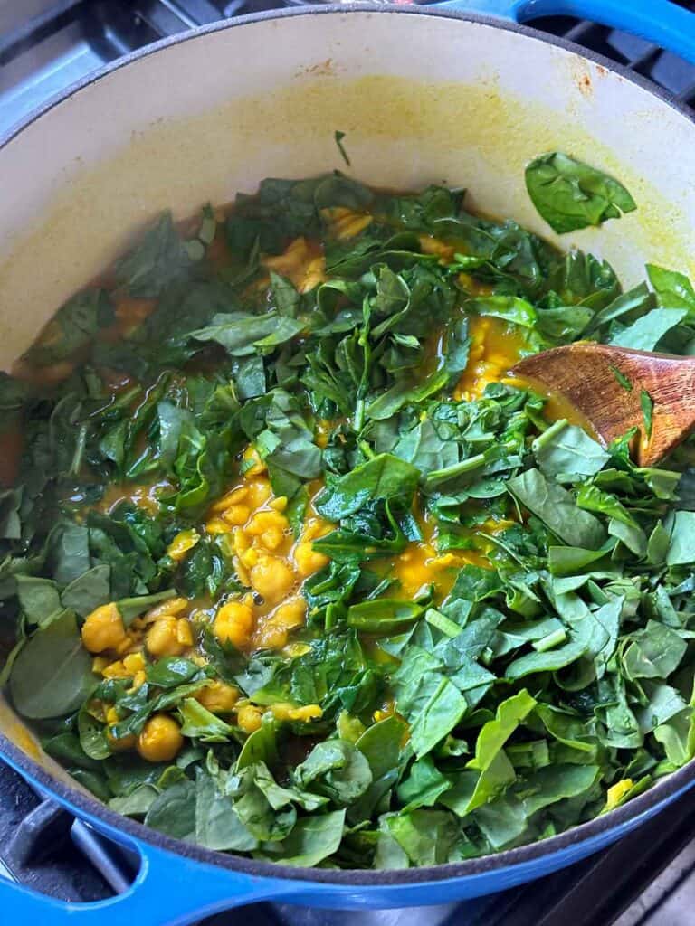 Adding spinach, cilantro, and parsley to turmeric soup to wilt in.