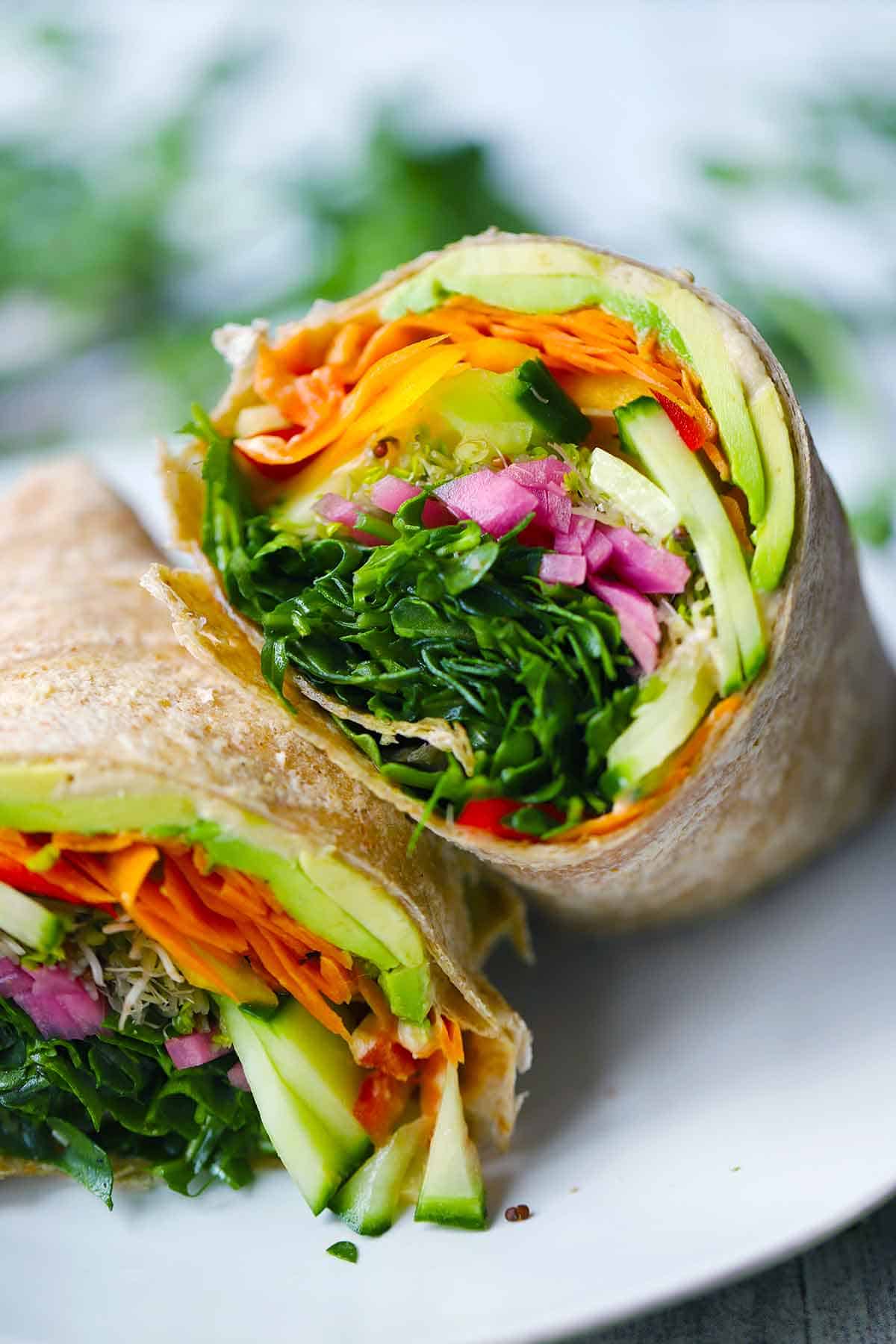 A veggie wrap cut in half on a white plate.