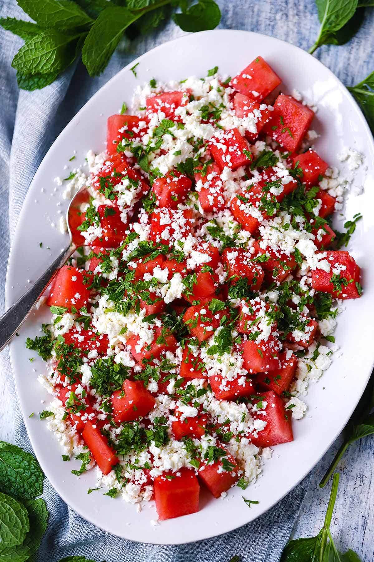 Overhead photo of a white platter with watermelon feta mint salad on it.