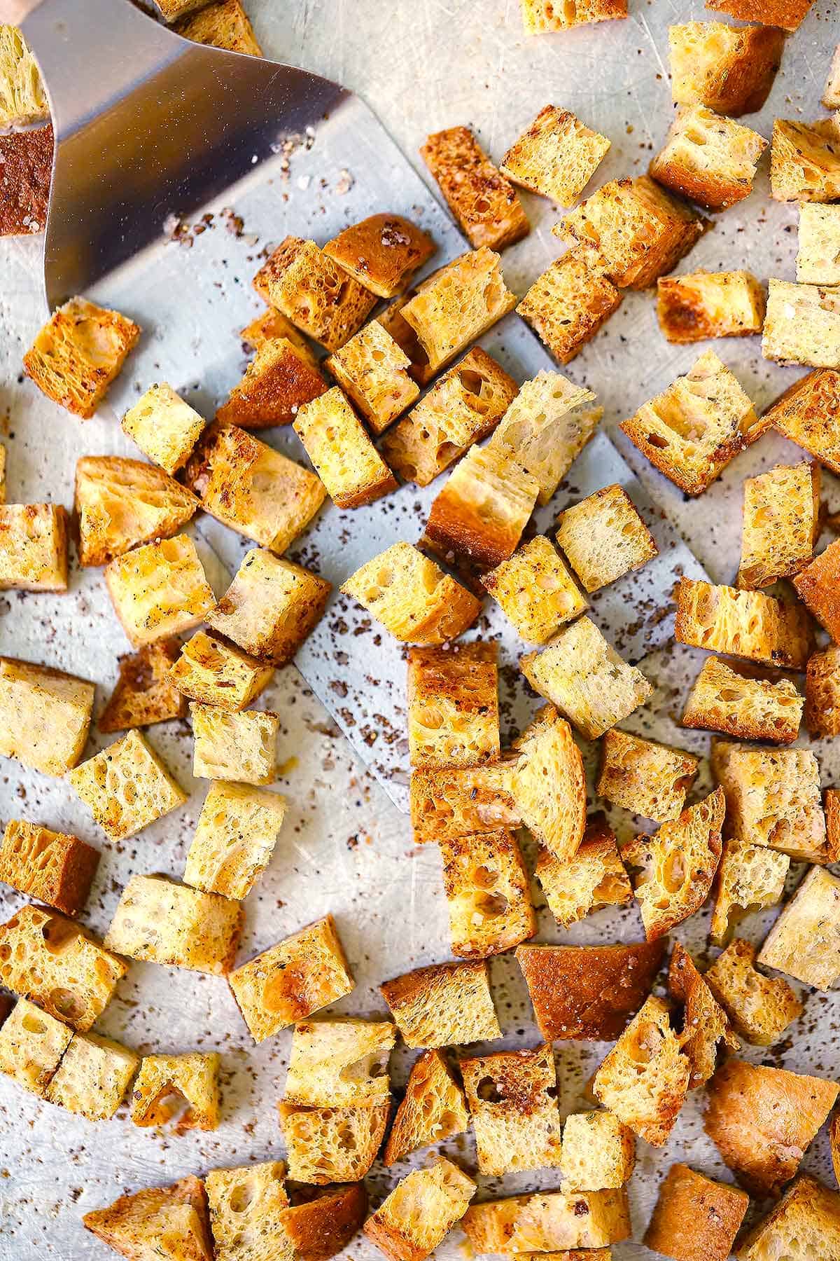 Overhead photo of a baking sheet with homemade croutons scattered on it.