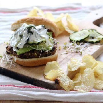 Black bean burger on a wooden cutting board with potato chips scattered around.