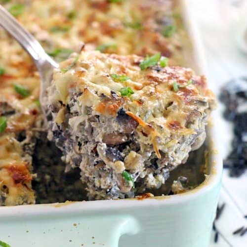 Metal spoon lifting a spoonful of casserole out of the corner of a ceramic casserole dish, filled with baked casserole.