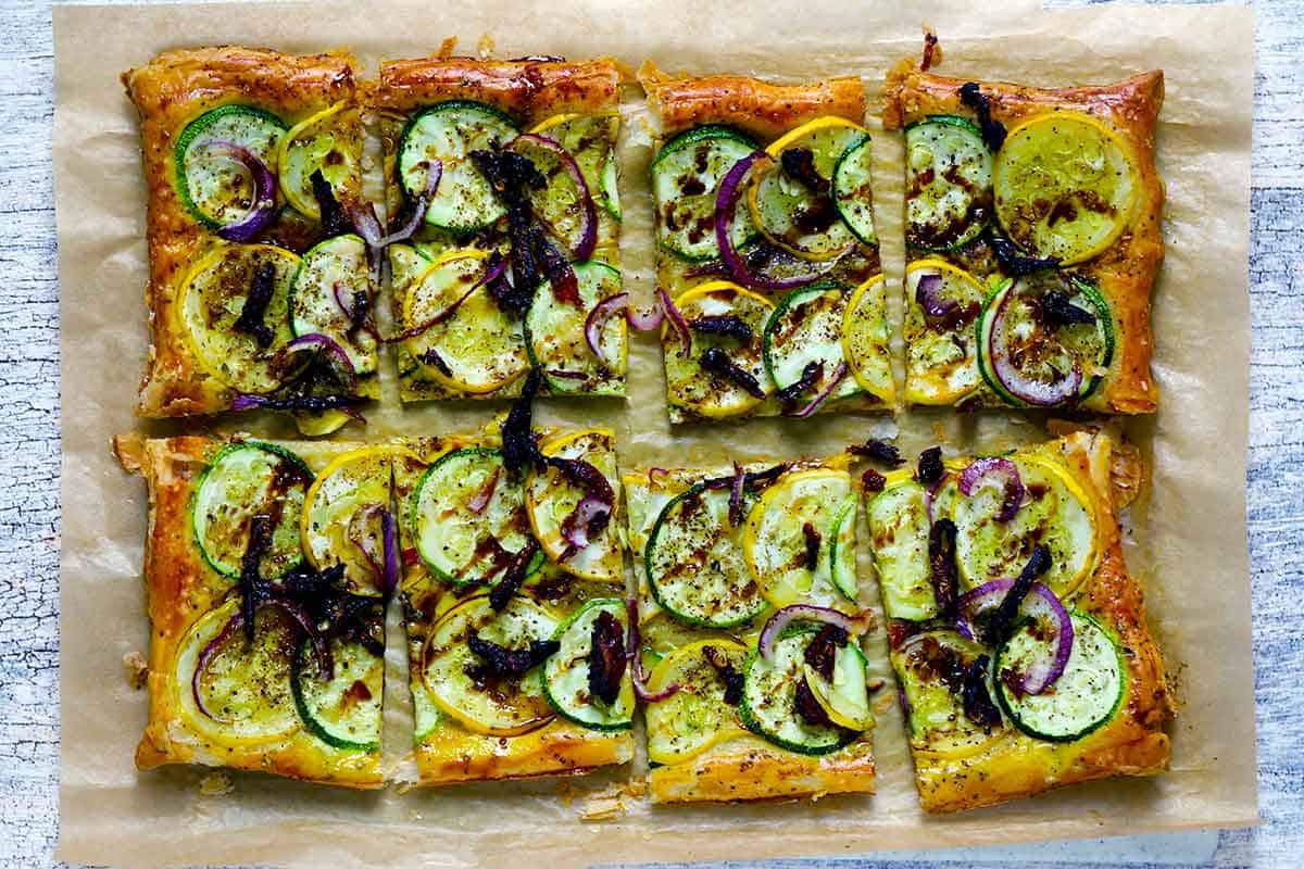 A puff pastry tart with zucchini and summer squash cut into eight pieces.
