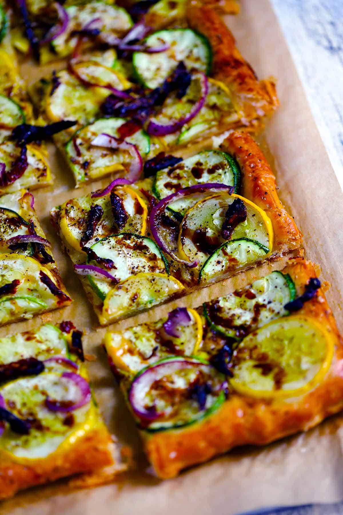 Close up photo of a slice of a puff pastry tart with zucchini and summer squash.